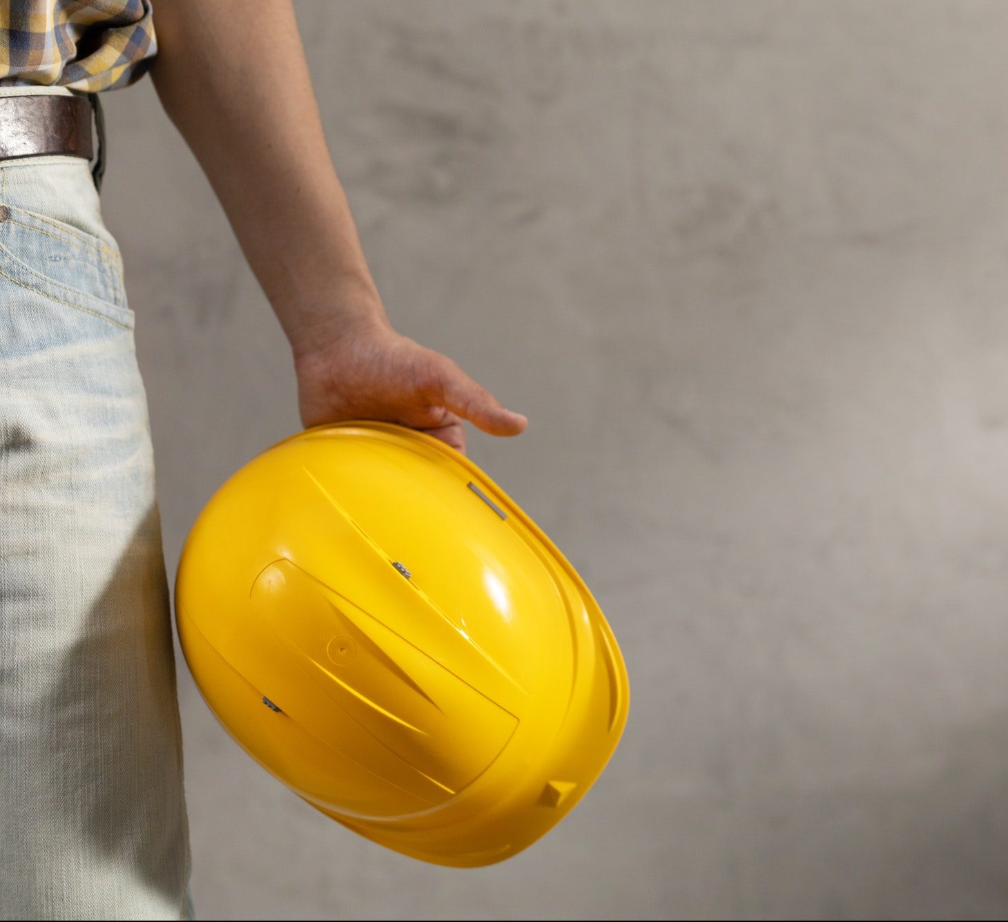 Worker man holding construction helmet tool near concrete or cement wall. Male hand and work cap